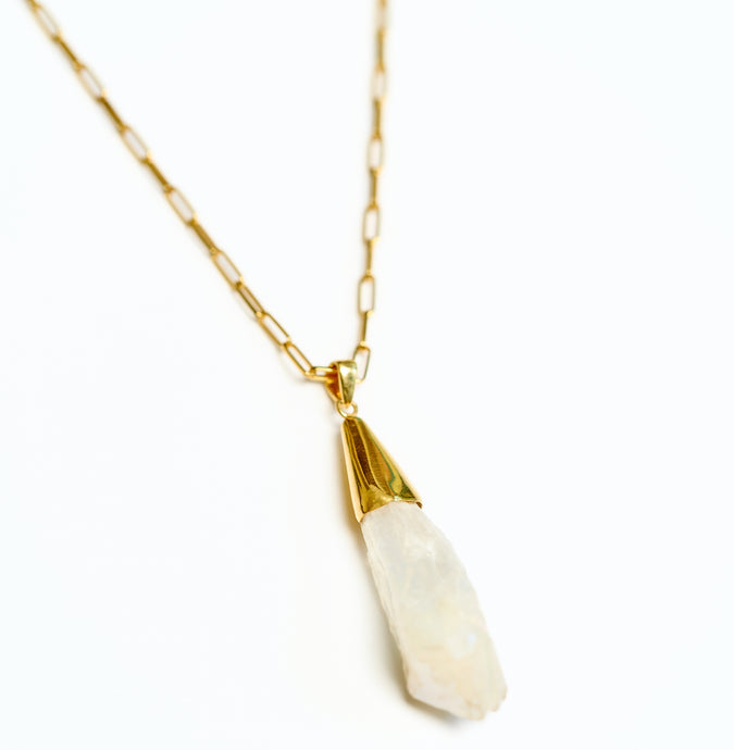 Gold chain necklace with a raw rock crystal pendant on a white background